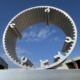 A circular, hollow aluminium heat sink against a sunny, blue sky from a low angle pointing skyward
