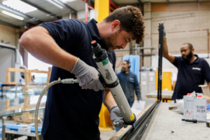 Male worker in a warehouse using an adhesive gun on an aluminium bar