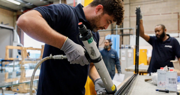 Male worker in a warehouse using an adhesive gun on an aluminium bar