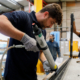 Male worker in a warehouse using an adhesive gun on an aluminium bar