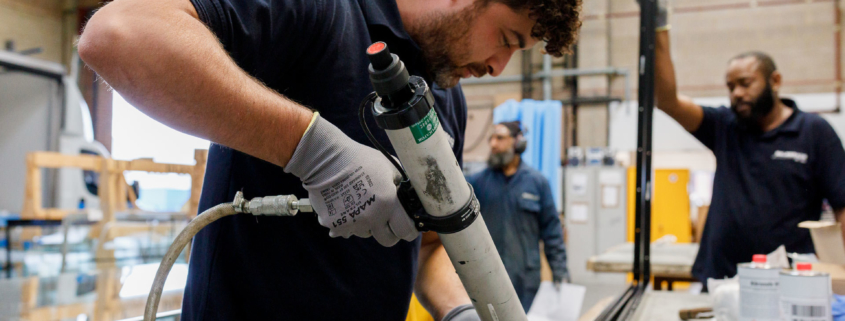 Male worker in a warehouse using an adhesive gun on an aluminium bar